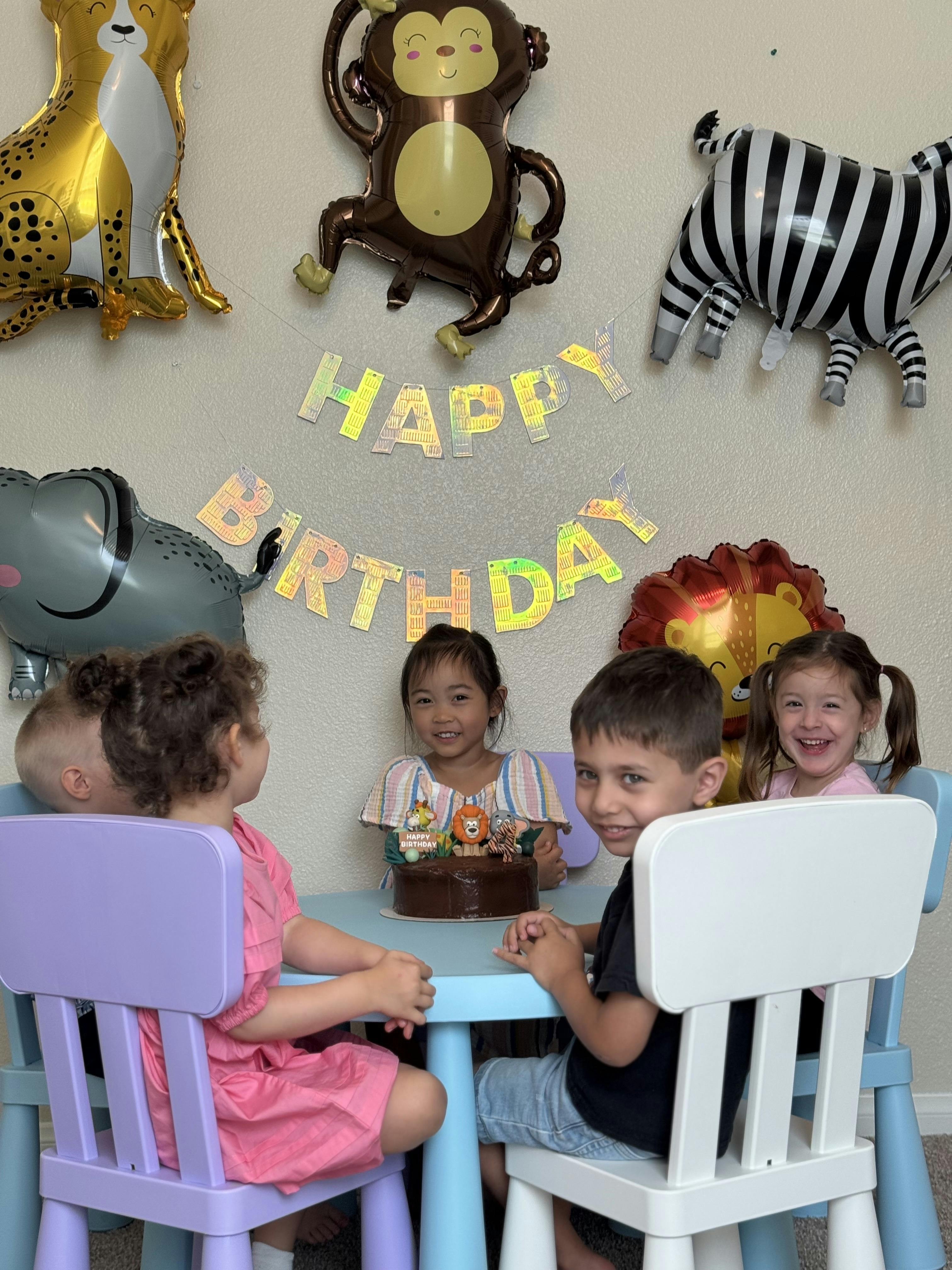 Children sitting around a table with a birthday cake and balloons