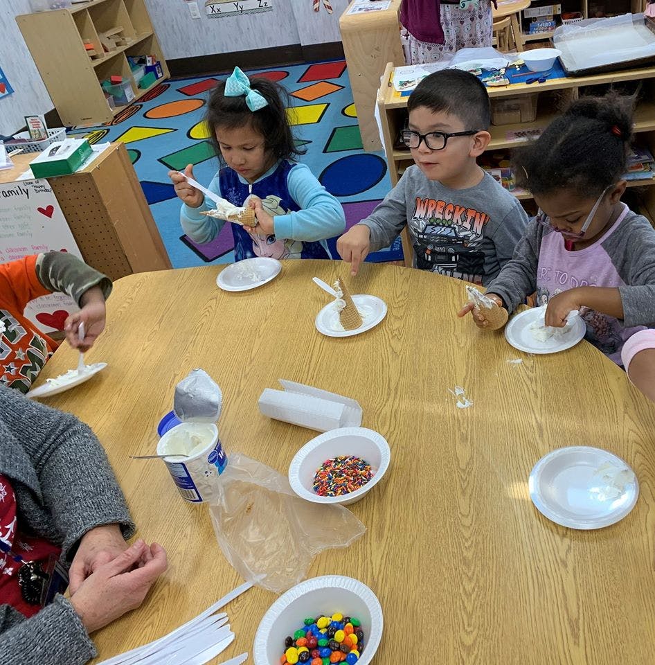 Children at a table with plates and bowls of sprinkles and candy
