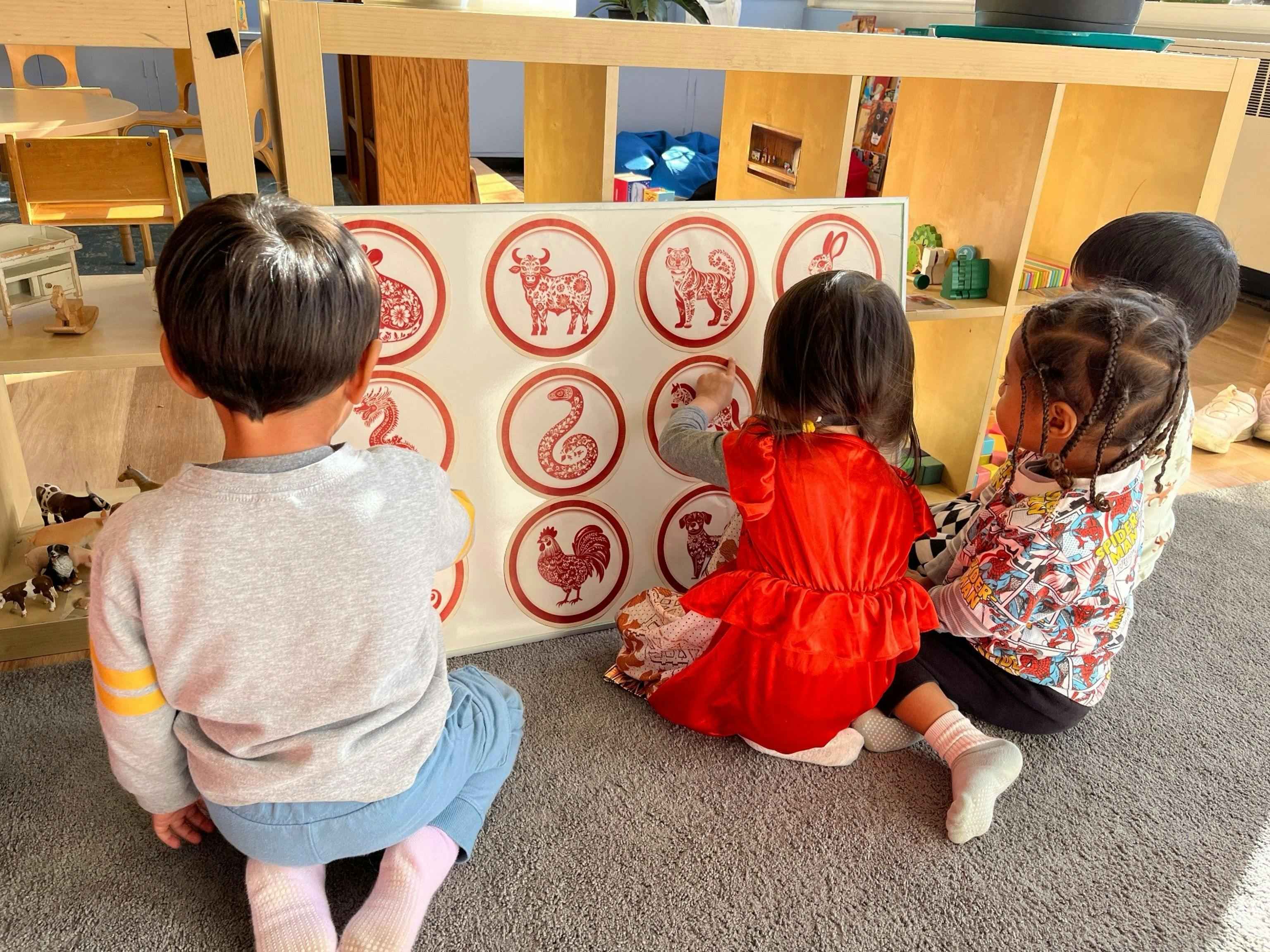 Three children sitting on the floor looking at a board with animal pictures