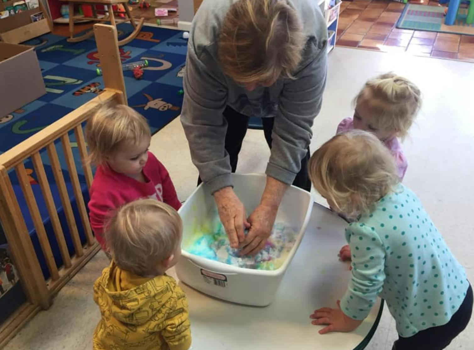 Person and three children playing with colorful water in a bin