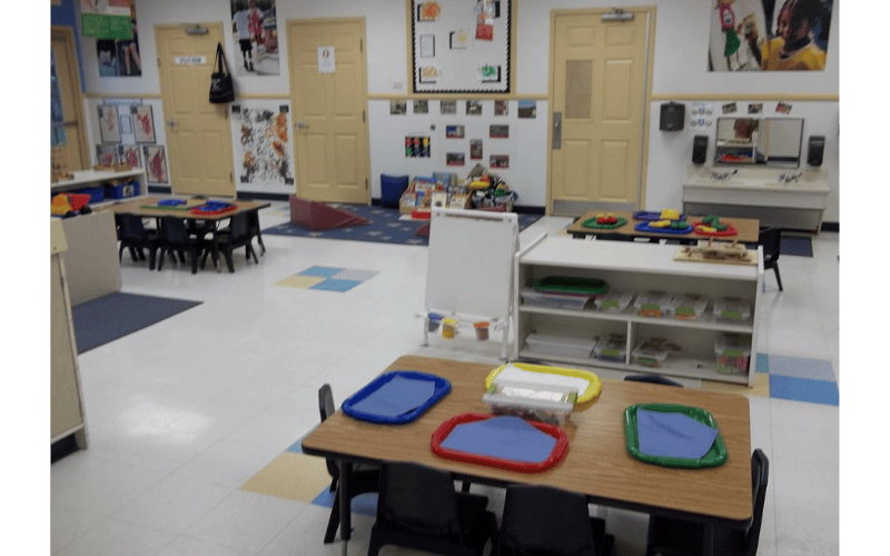 An empty classroom with multiple tables, chairs, and learning materials