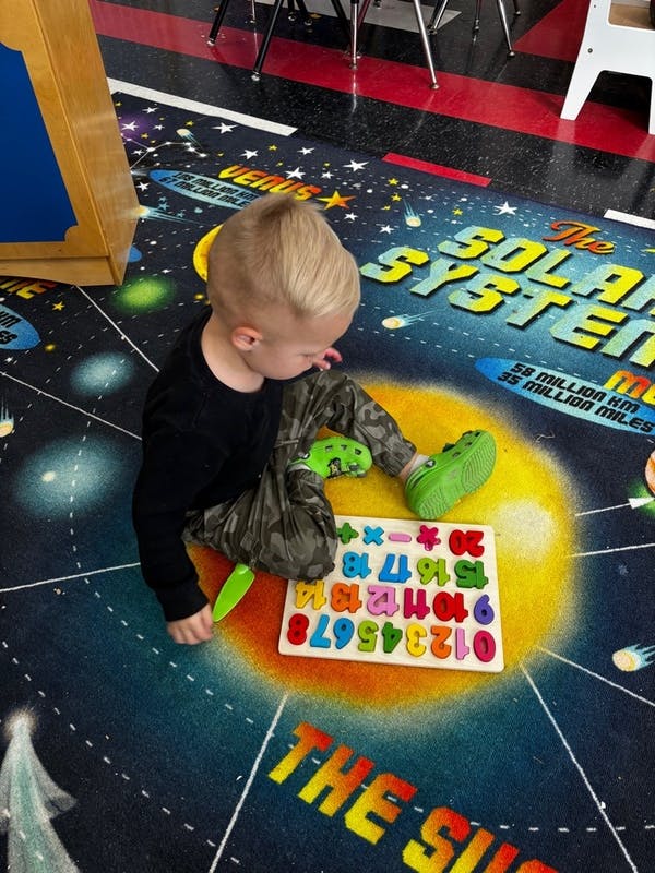 Child playing with a number and letter puzzle on a solar system rug