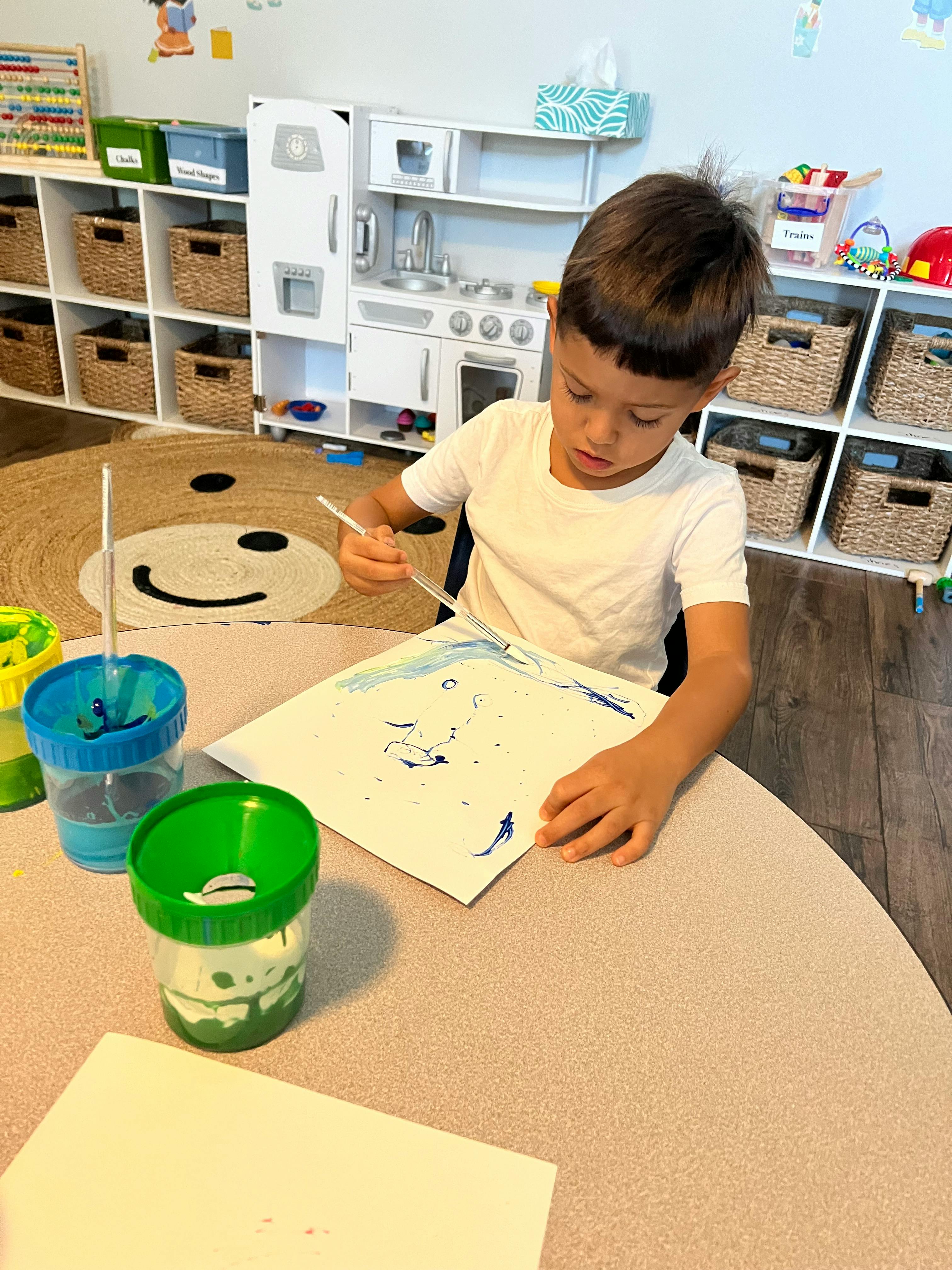 Child painting with a brush on paper at a table in a classroom