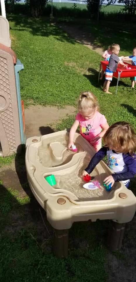 Two children playing with water and toys at a water table