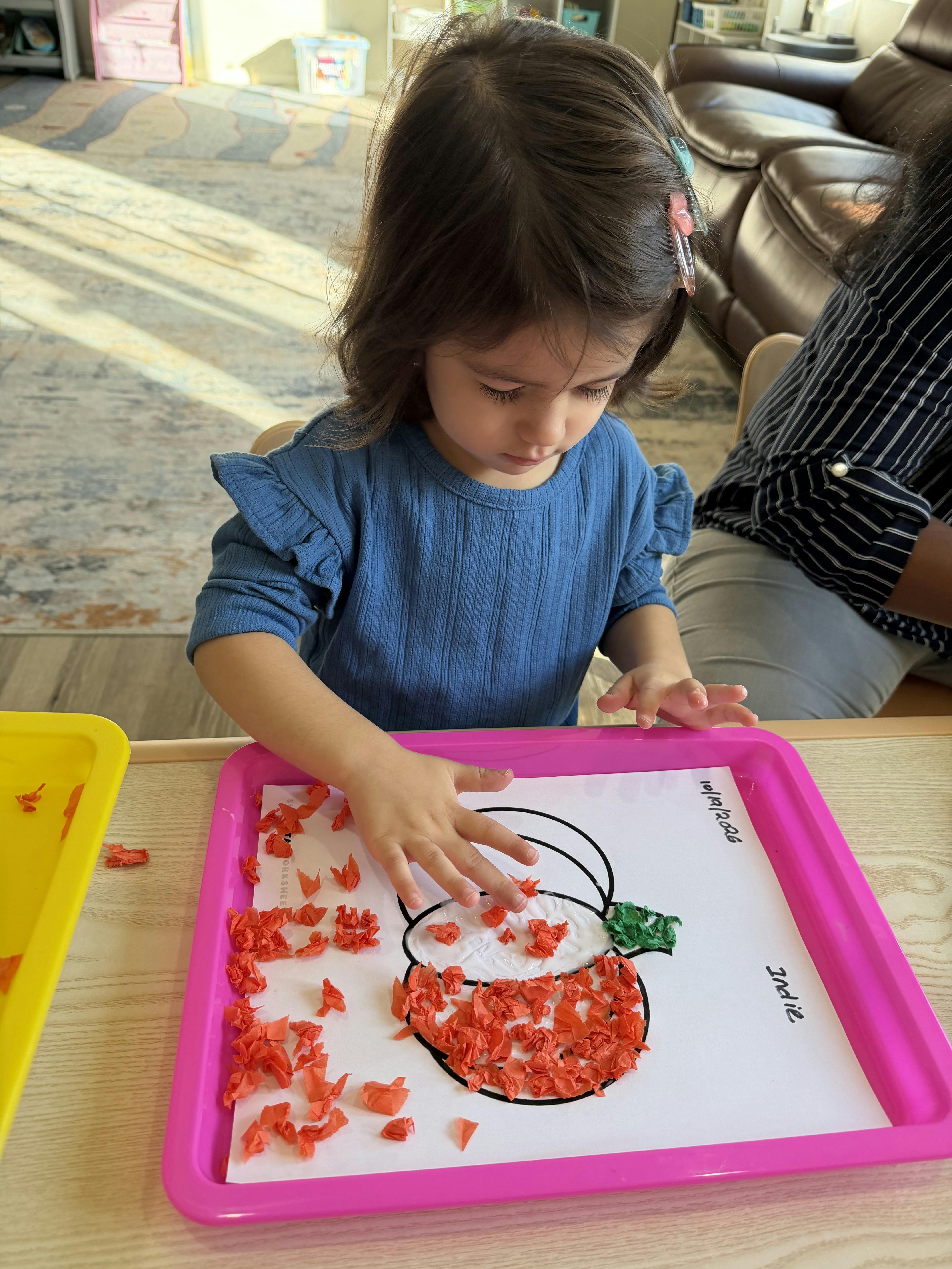 Child gluing red paper pieces onto a pumpkin craft worksheet