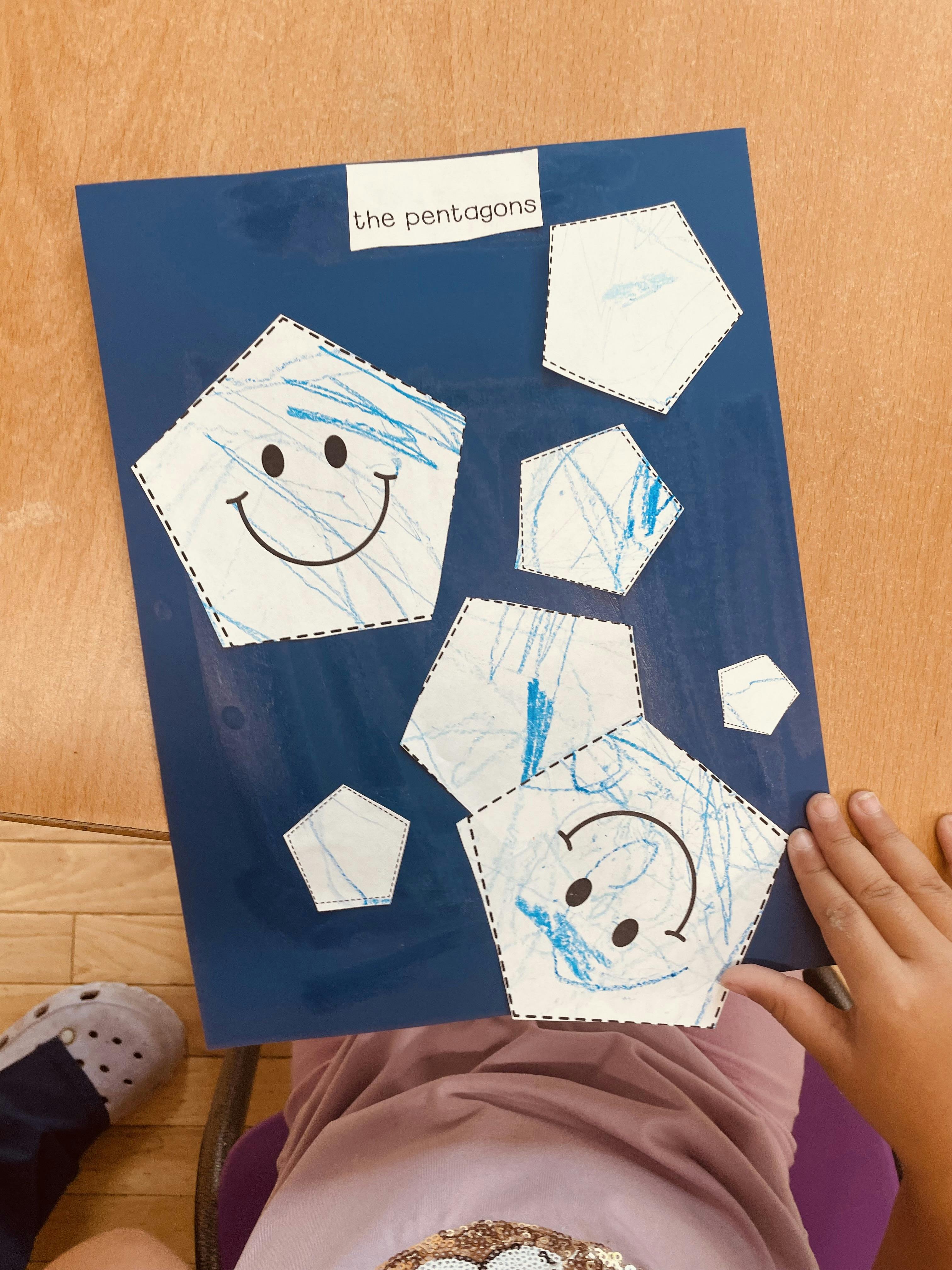 Child holding a blue paper craft titled the pentagons
