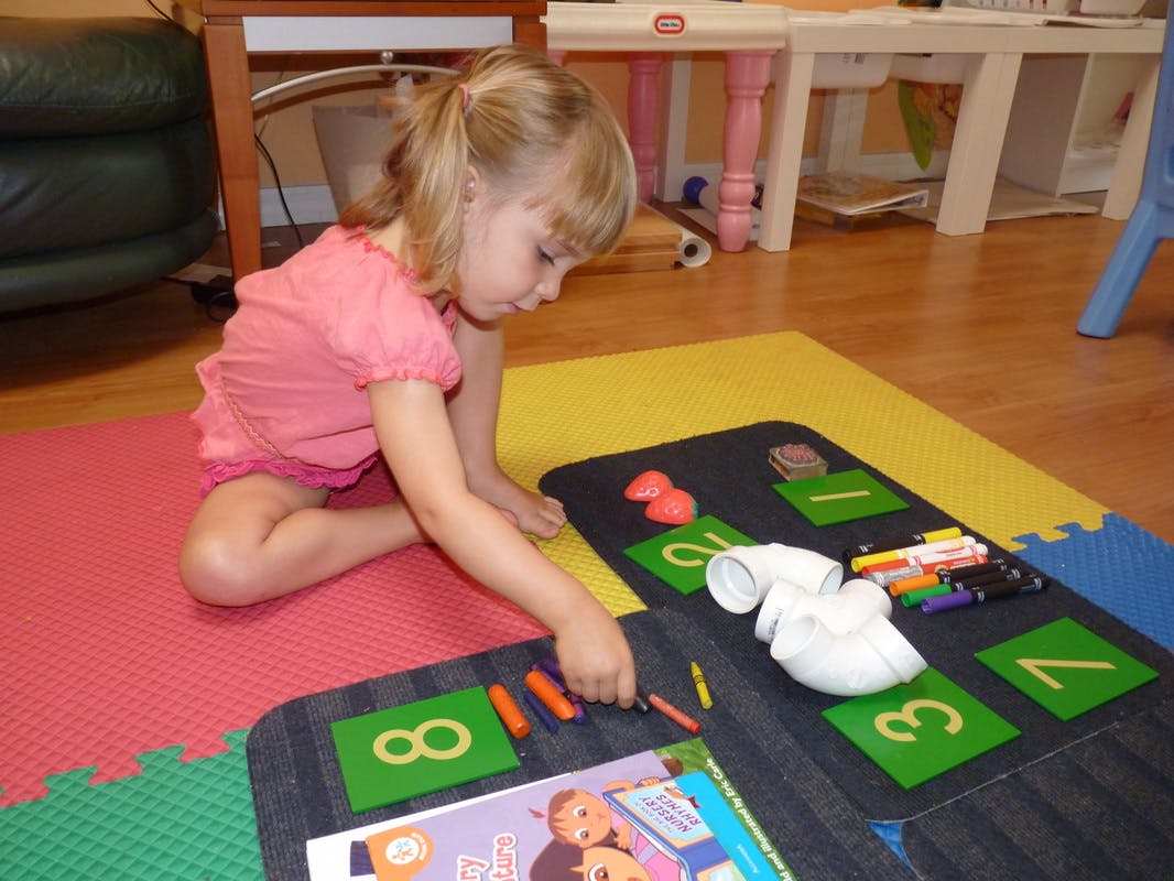 Child sitting on floor playing with crayons and number cards