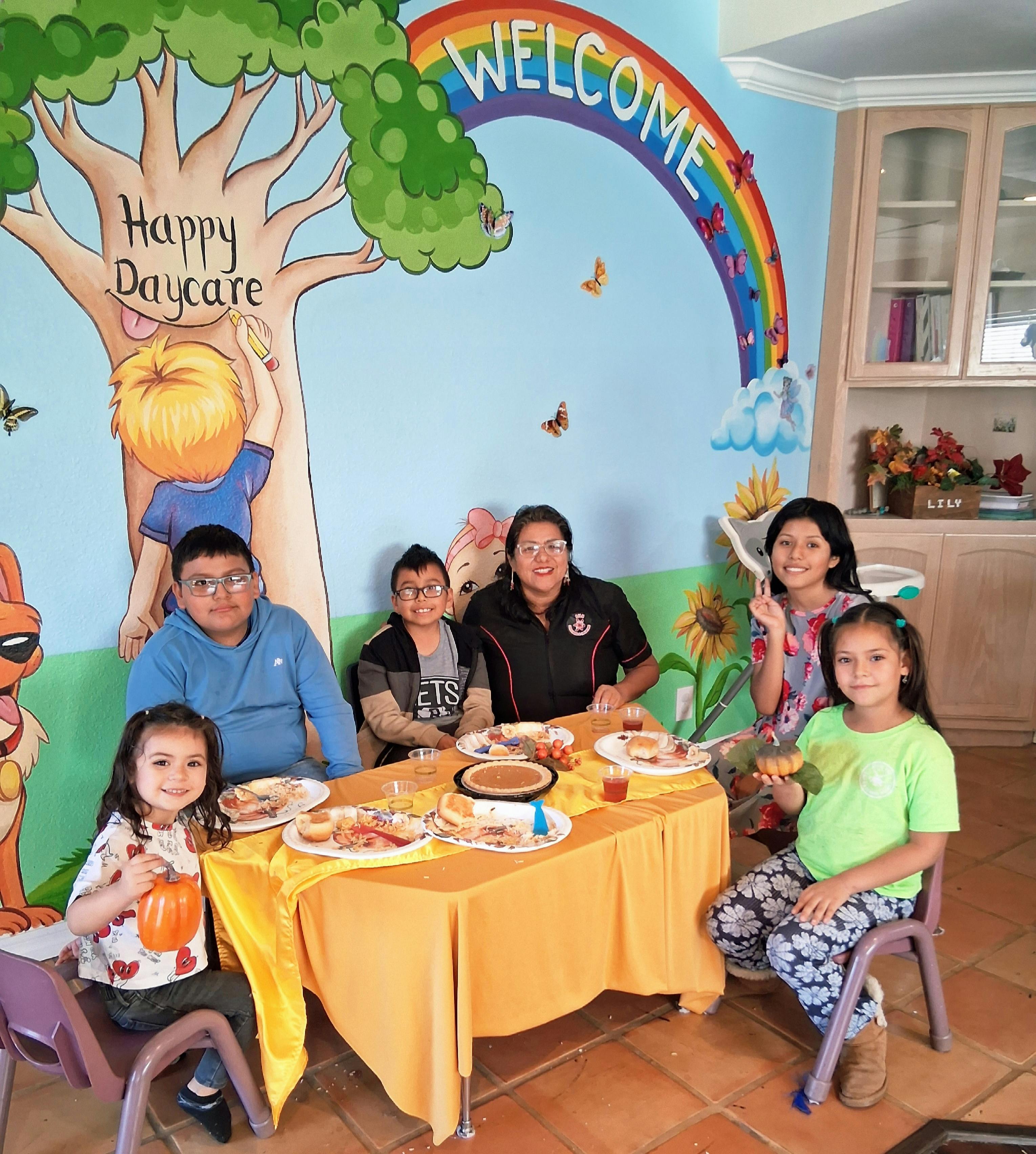 An adult and five children sitting around a table with food in a daycare