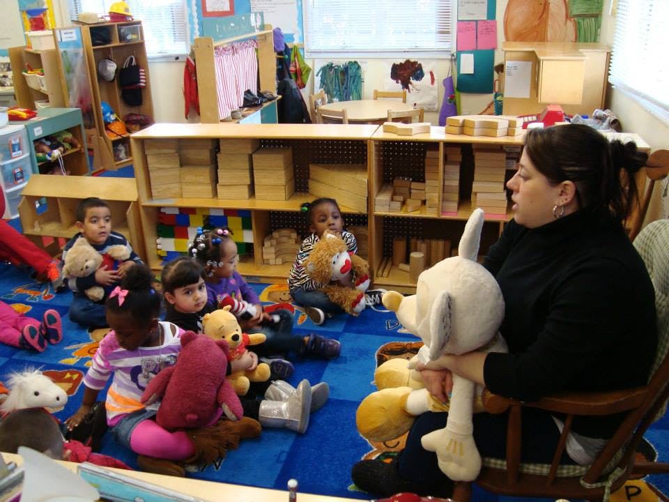 Adult holding a stuffed animal reading to children in a classroom