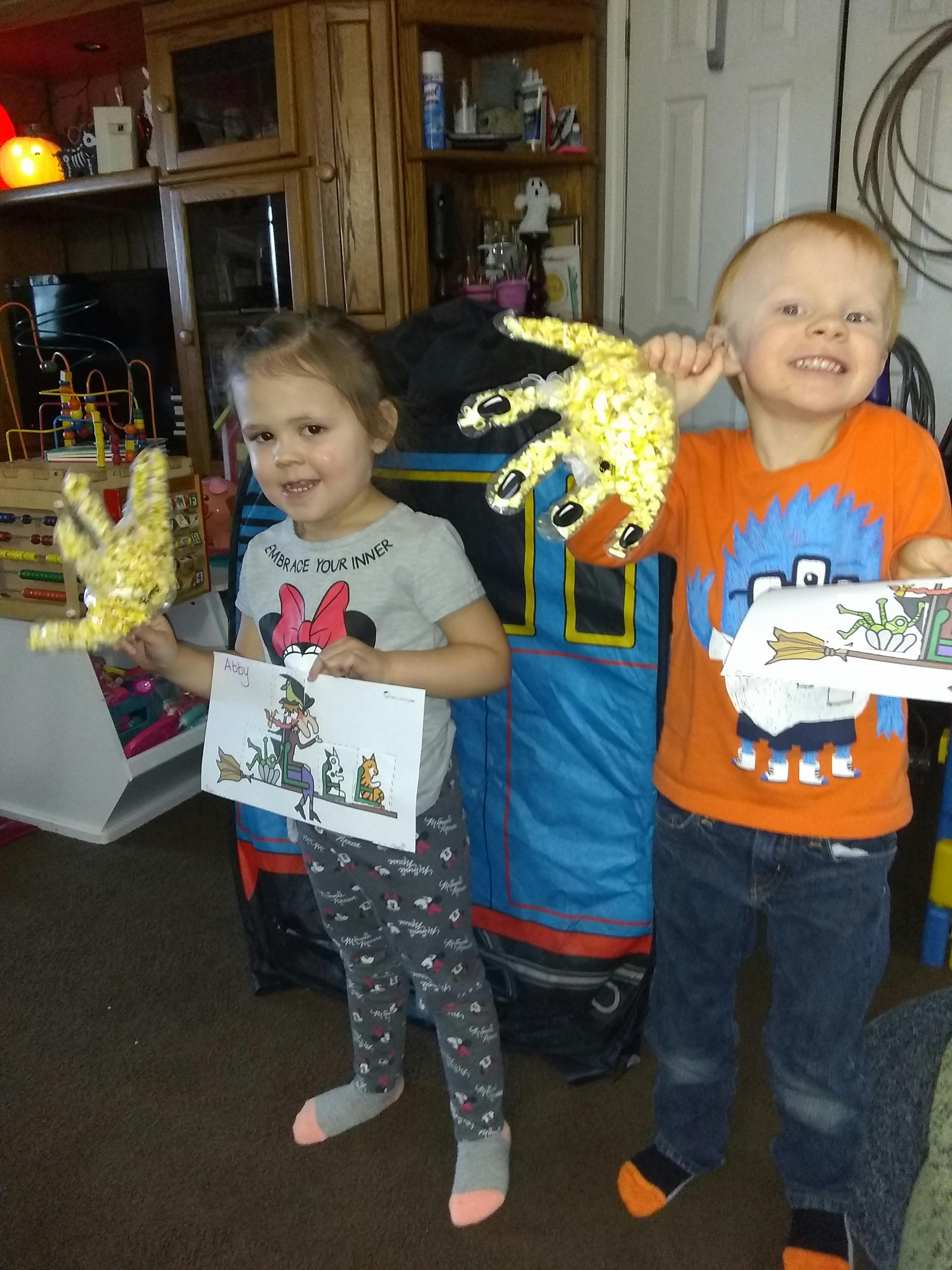 Two children holding up crafts and displaying their artwork
