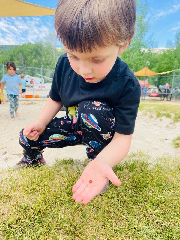 Child crouching and holding a small red object in an open palm