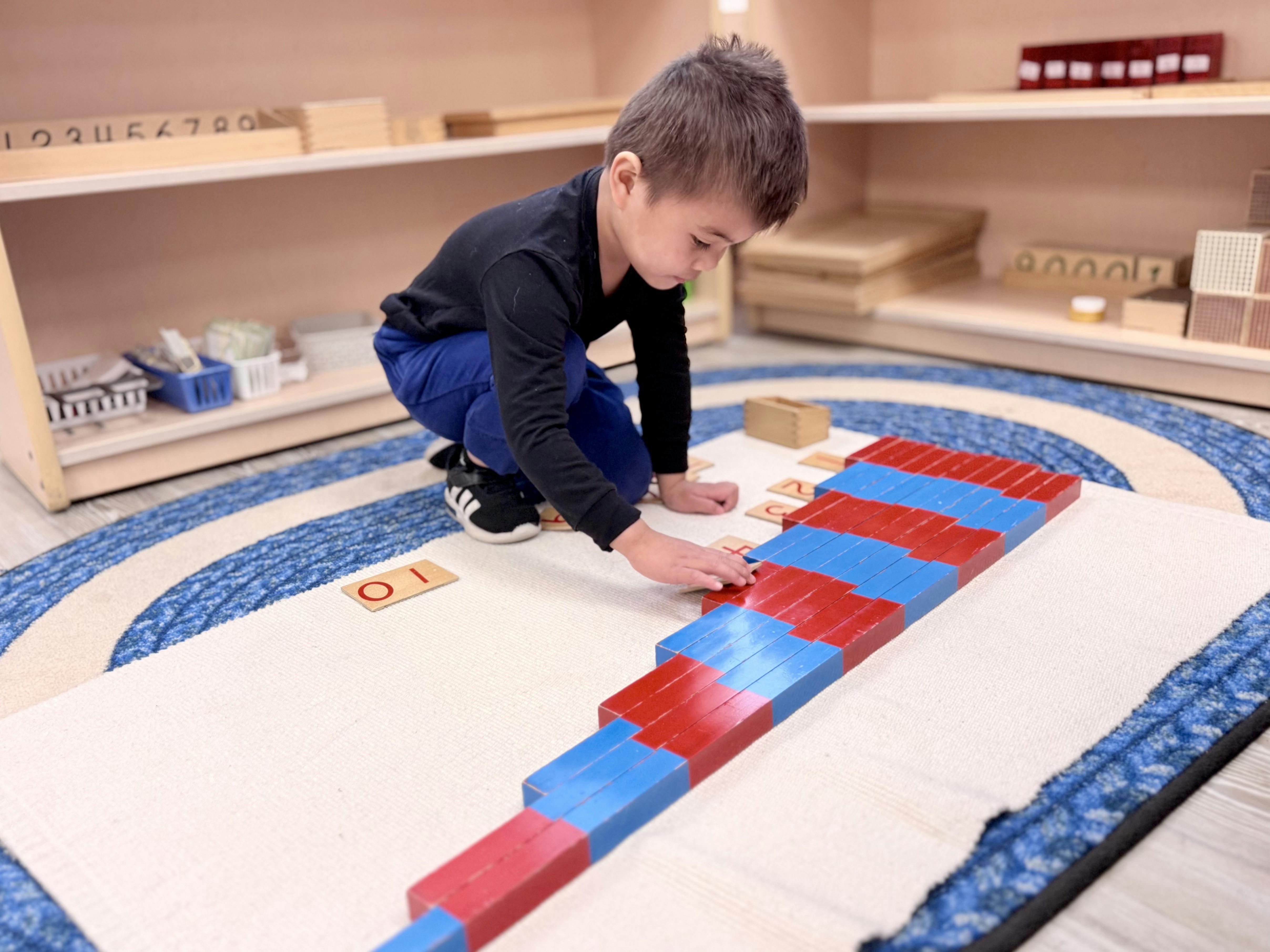 Child crouching and placing red and blue blocks on a rug