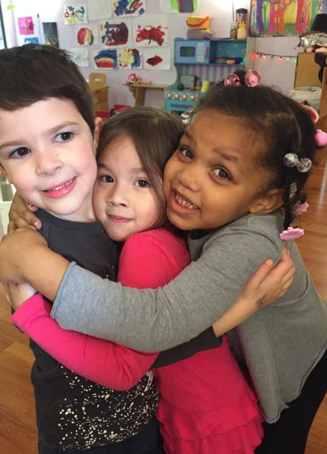 Three children hugging in a classroom