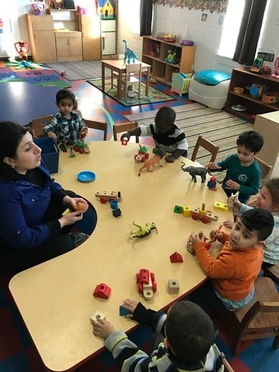 Adult and children playing with toys at a table in a classroom