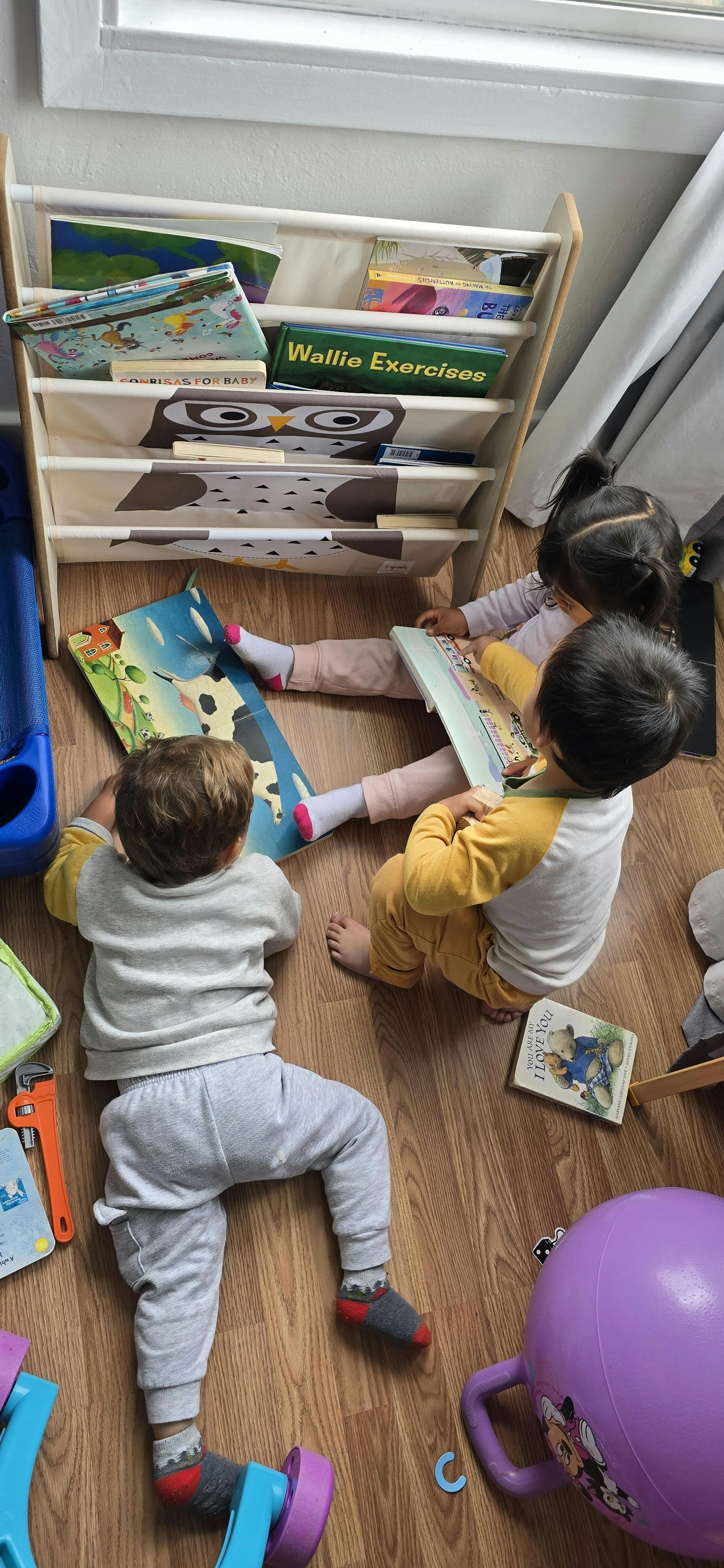 Three young children reading books on the floor next to a bookshelf