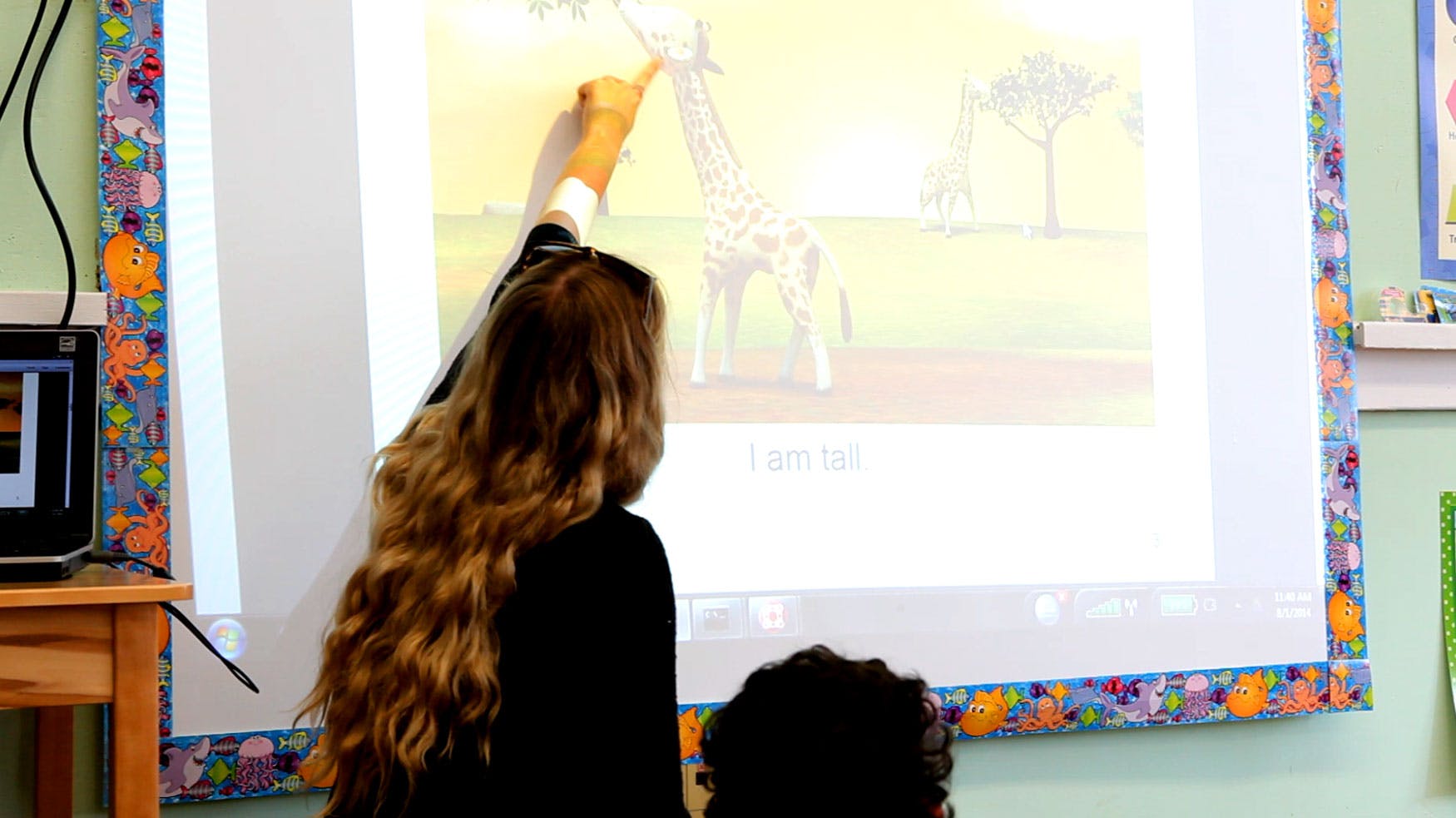 Person pointing at a giraffe illustration on a screen in a classroom