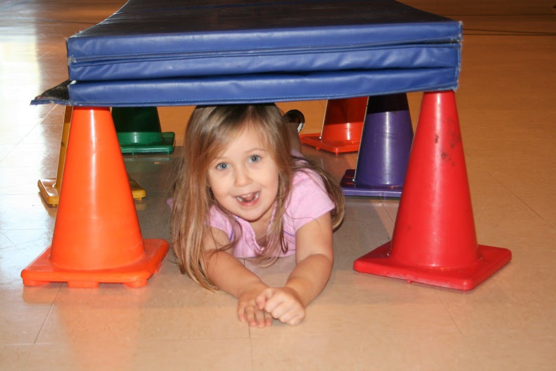 Child crawling under a blue mat supported by traffic cones