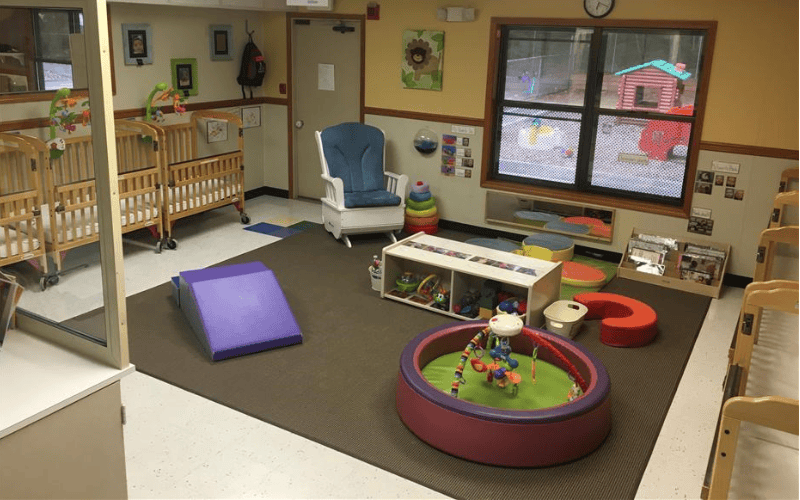 A playroom with cribs, a rocking chair, toys, and a window looking out to an outdoor playhouse