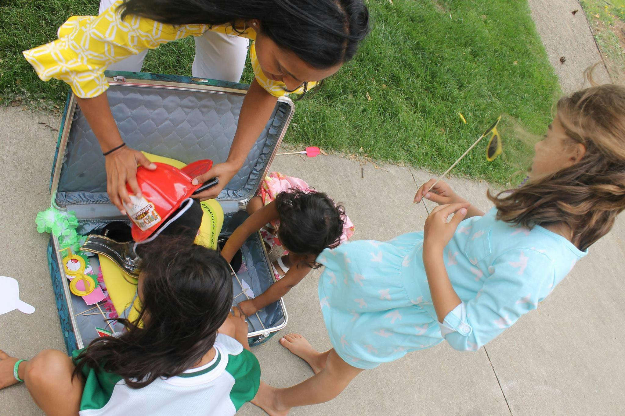 Three children playing with items in an open suitcase