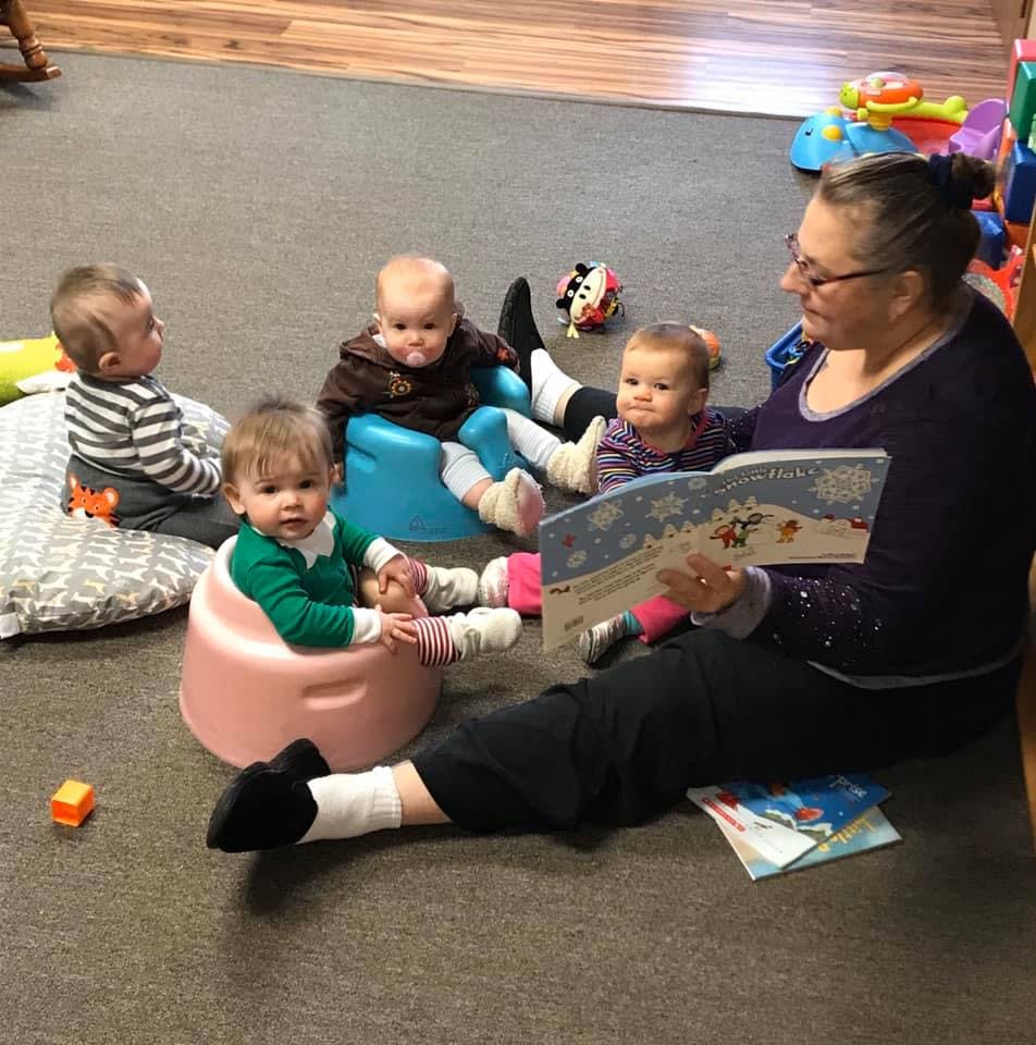 Person reading a book to multiple children sitting on the floor