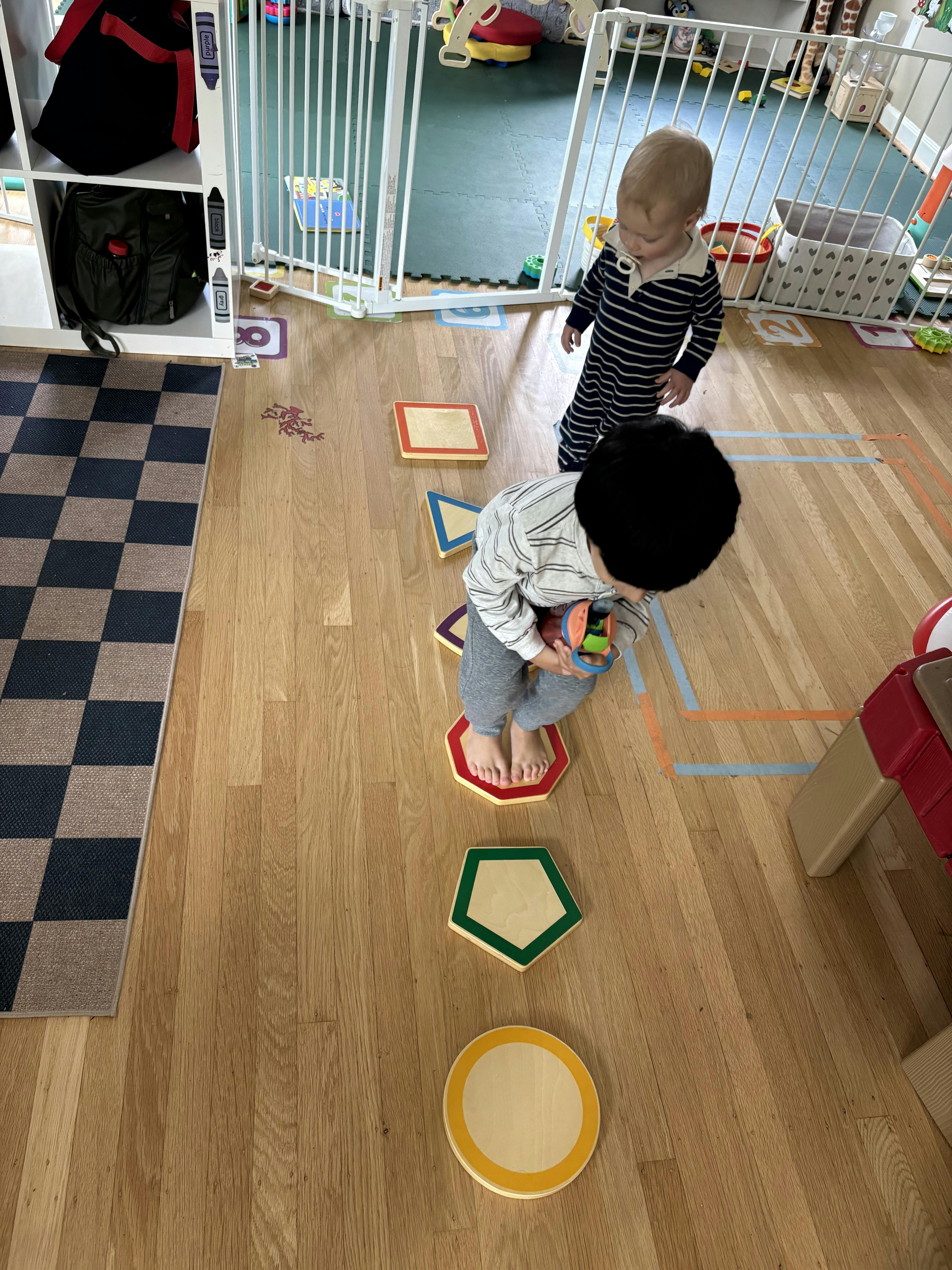 Two children playing on a wooden floor with shape cutouts