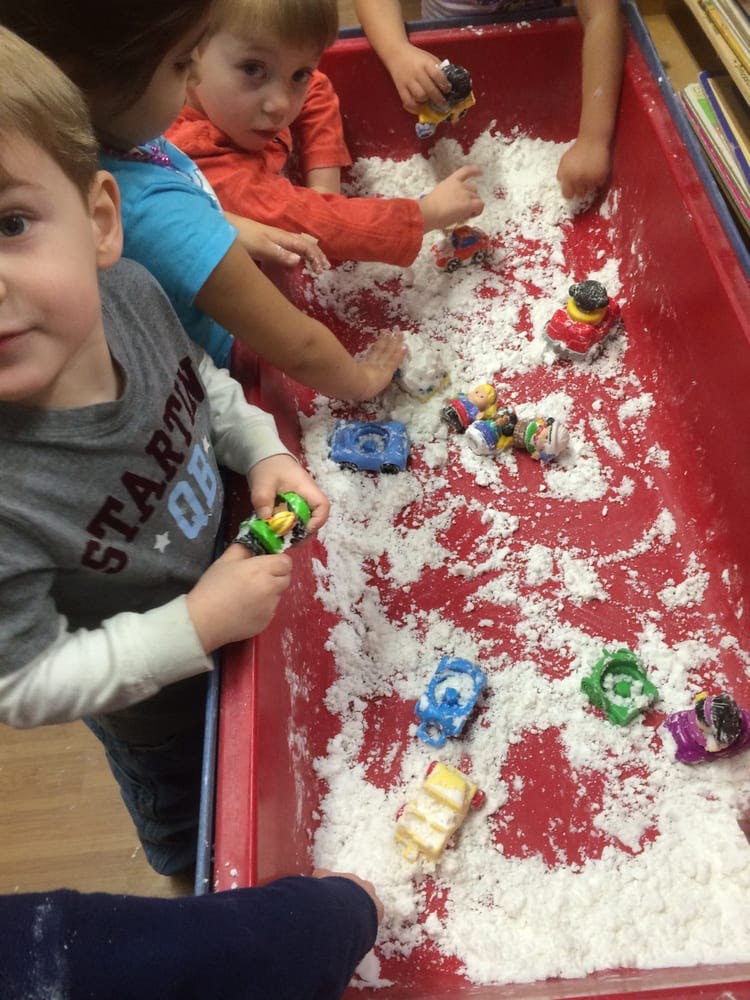 Children playing with toy cars in a red bin filled with white material