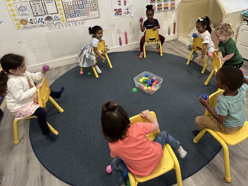 Group of children seated in a circle playing with colorful balls
