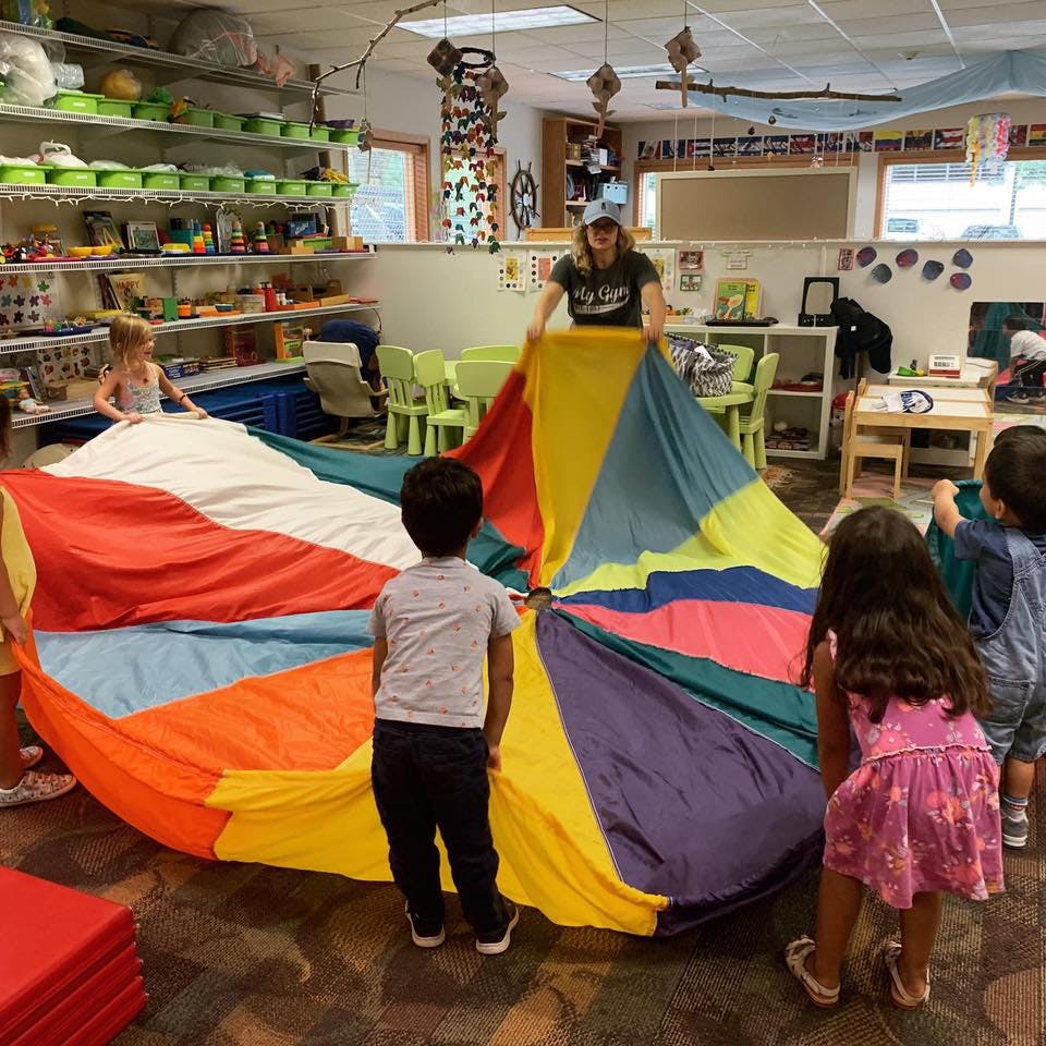 Person and children playing with a colorful parachute in a classroom