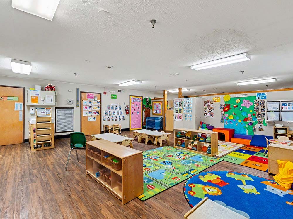 A colorful children's play area with activity rugs, small tables, and toy storage