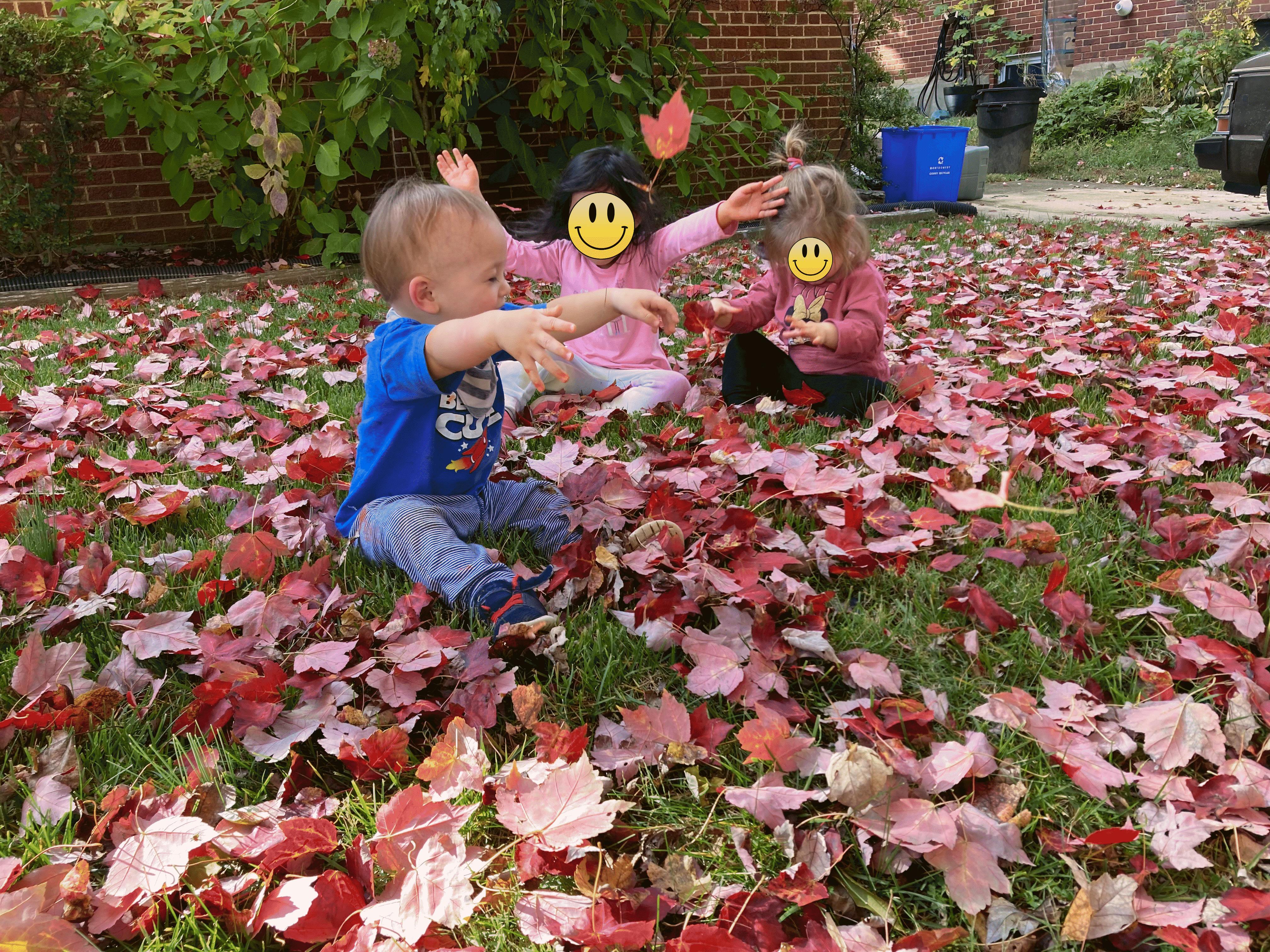 Three children playing with autumn leaves in a yard