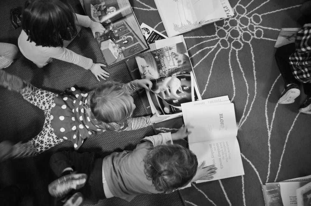 Three children looking at books on the floor