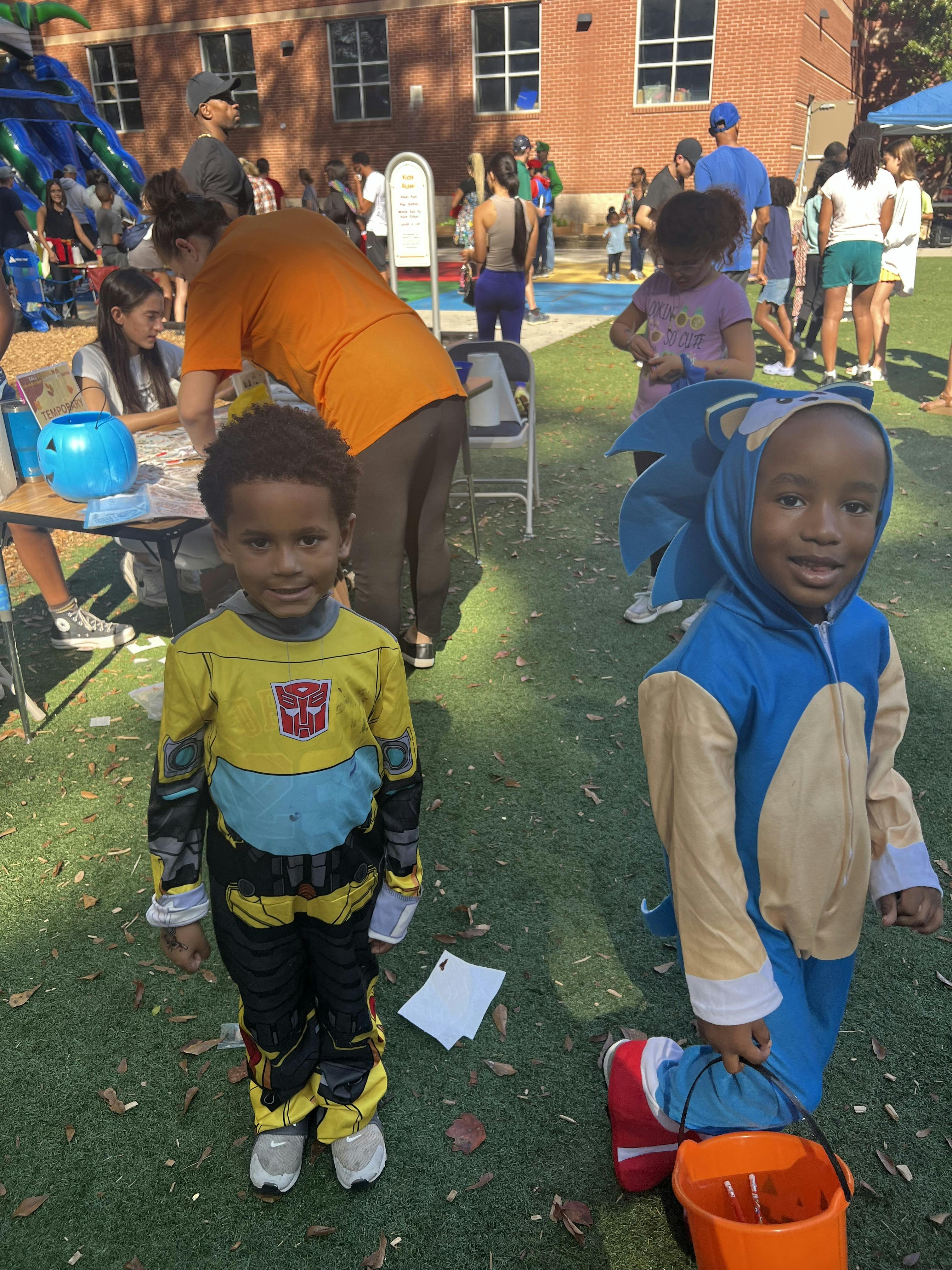 Two children in costumes standing on grass, one in Bumblebee and one in Sonic