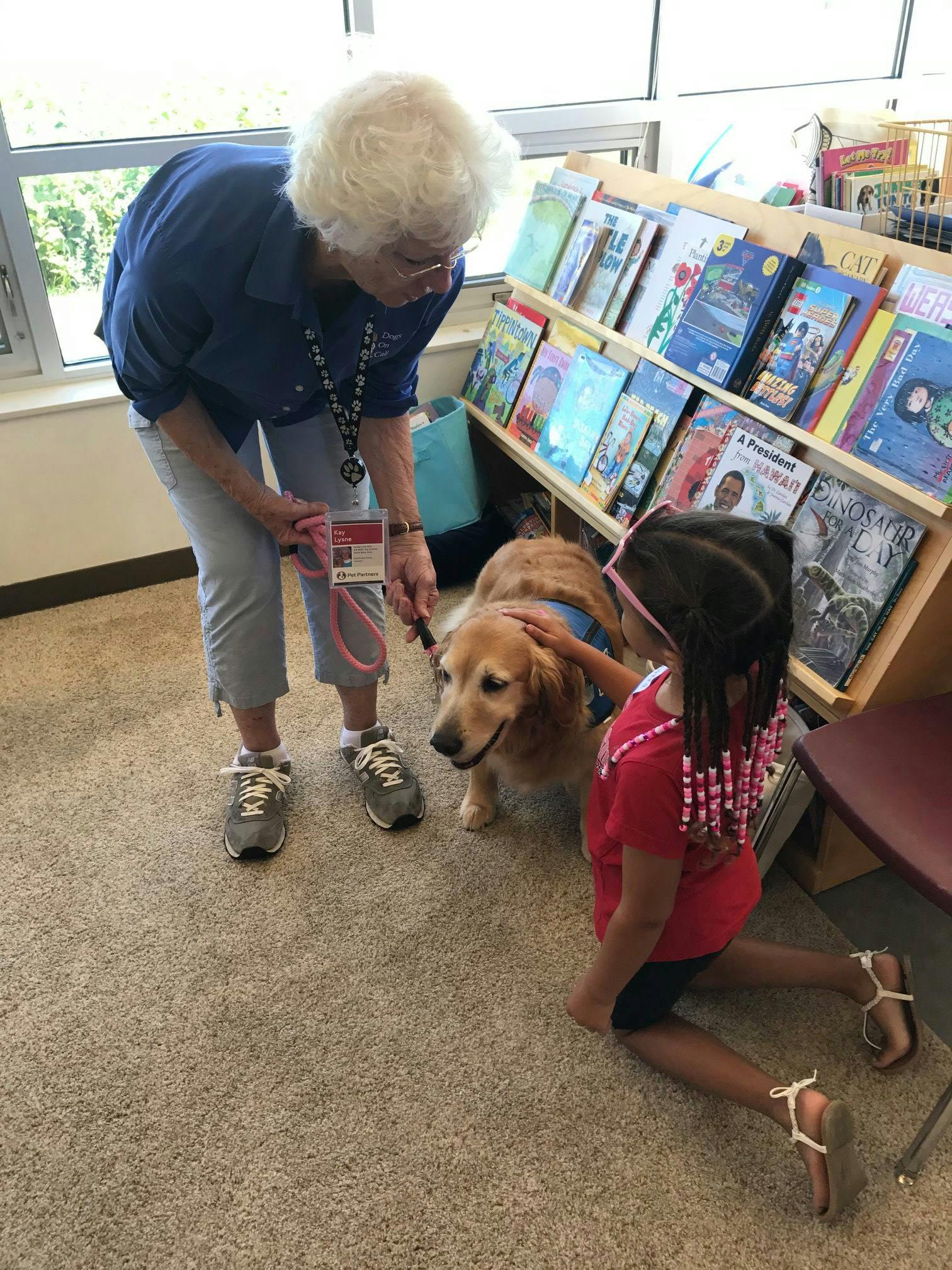 Adult and child petting a golden retriever in a room with books