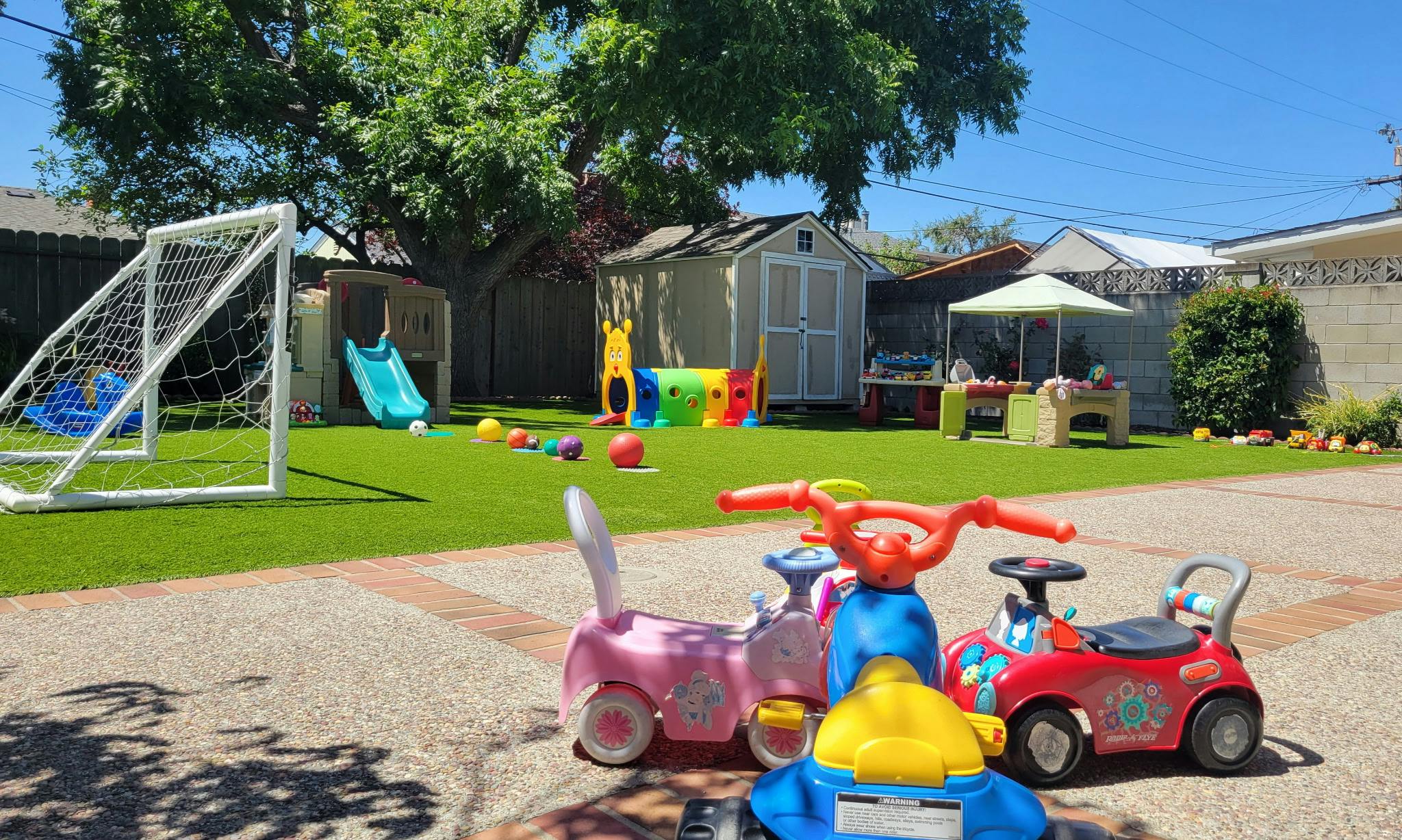 Backyard play area with toy ride-on cars, a soccer goal, and a slide