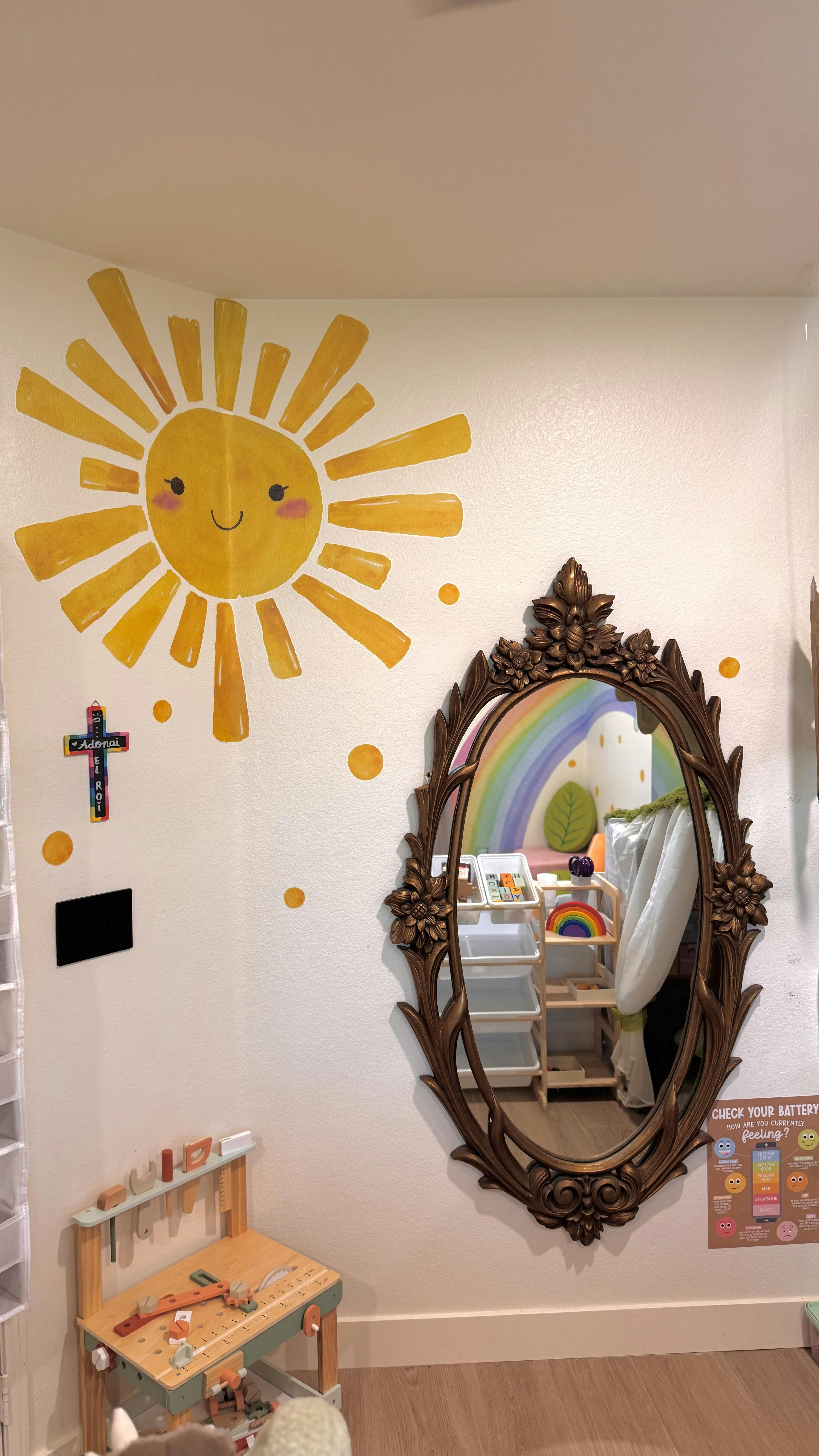 Decorative sun mural and ornate mirror on a wall in a child's playroom