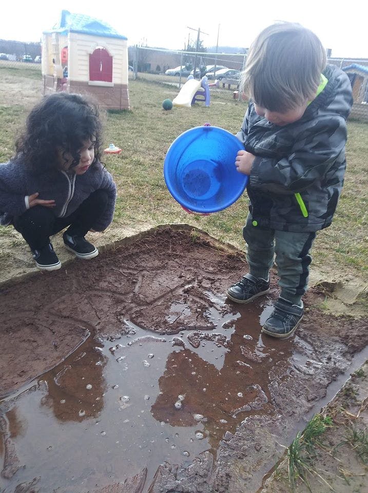 Two children playing in mud with a blue bucket