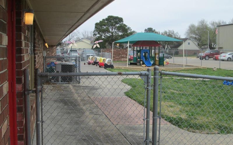 A fenced outdoor play area with small cars and a covered playground structure