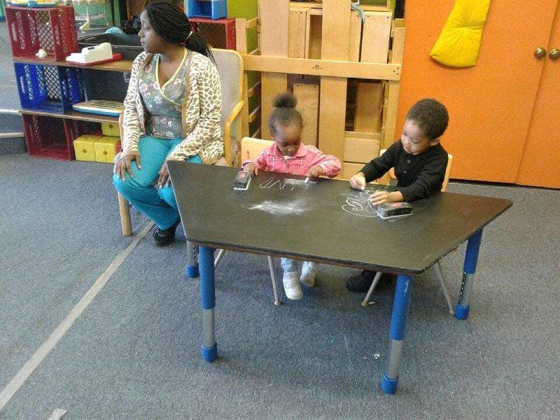 Person sitting at a table with two children drawing on it