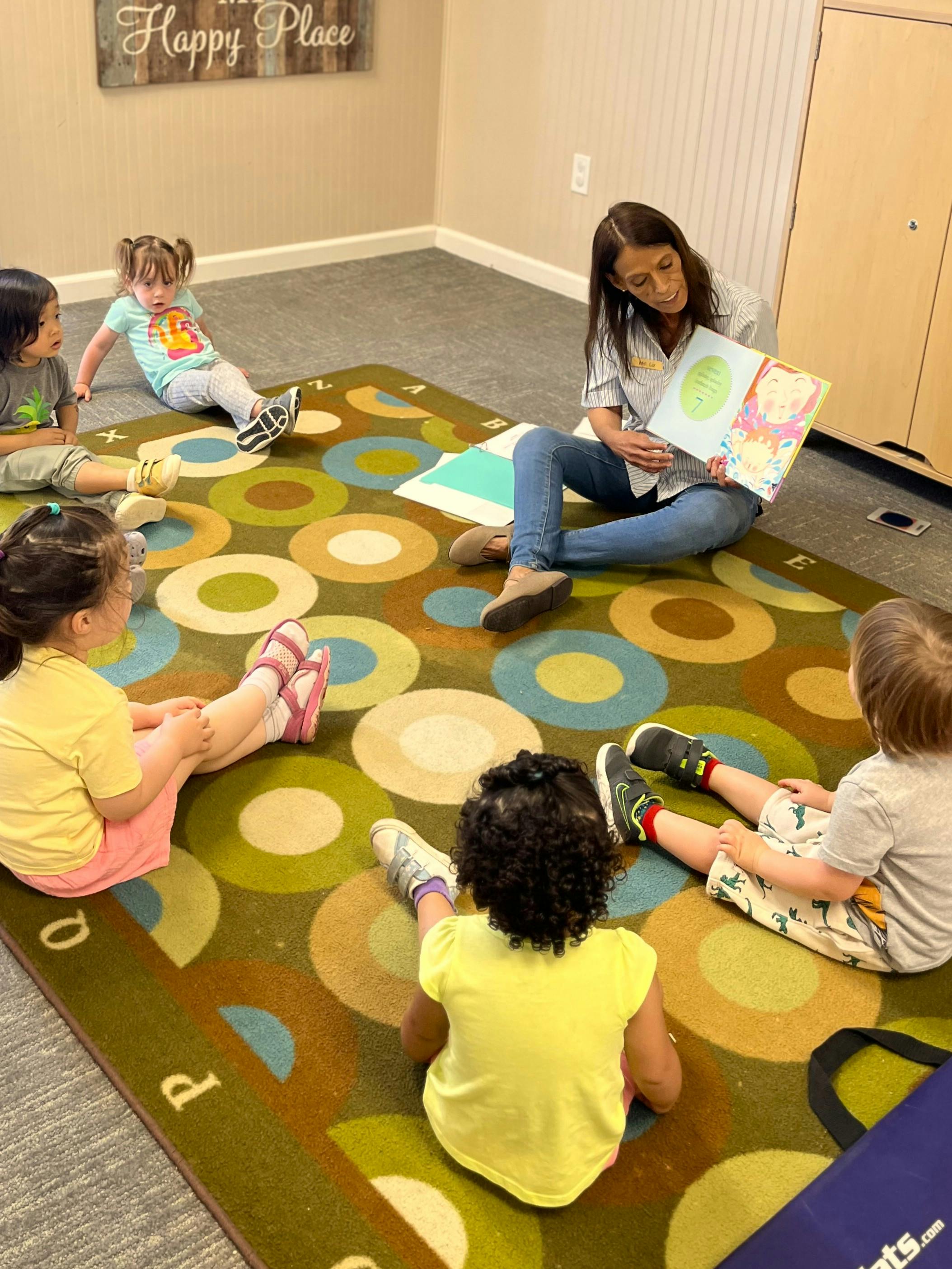 Adult reading a book to a group of children sitting on a colorful rug