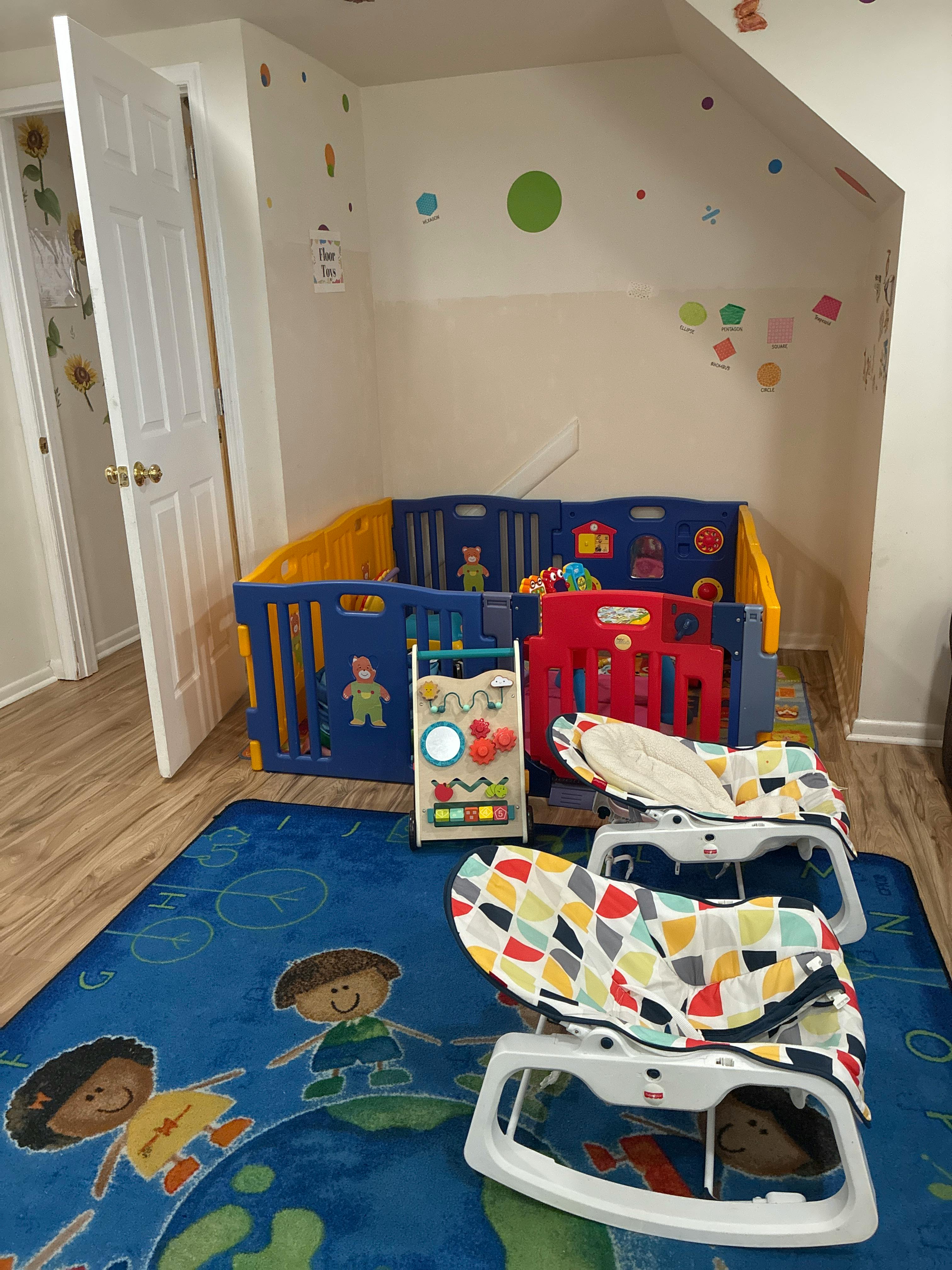 Baby play area with a colorful playpen, bouncer, activity board, and patterned rug