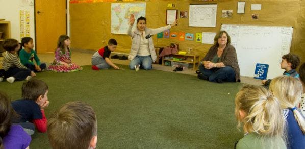 Adults and children sitting on a green rug in a classroom