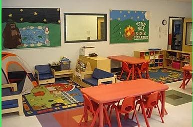 Classroom with small tables and chairs, play tent, and colorful rugs