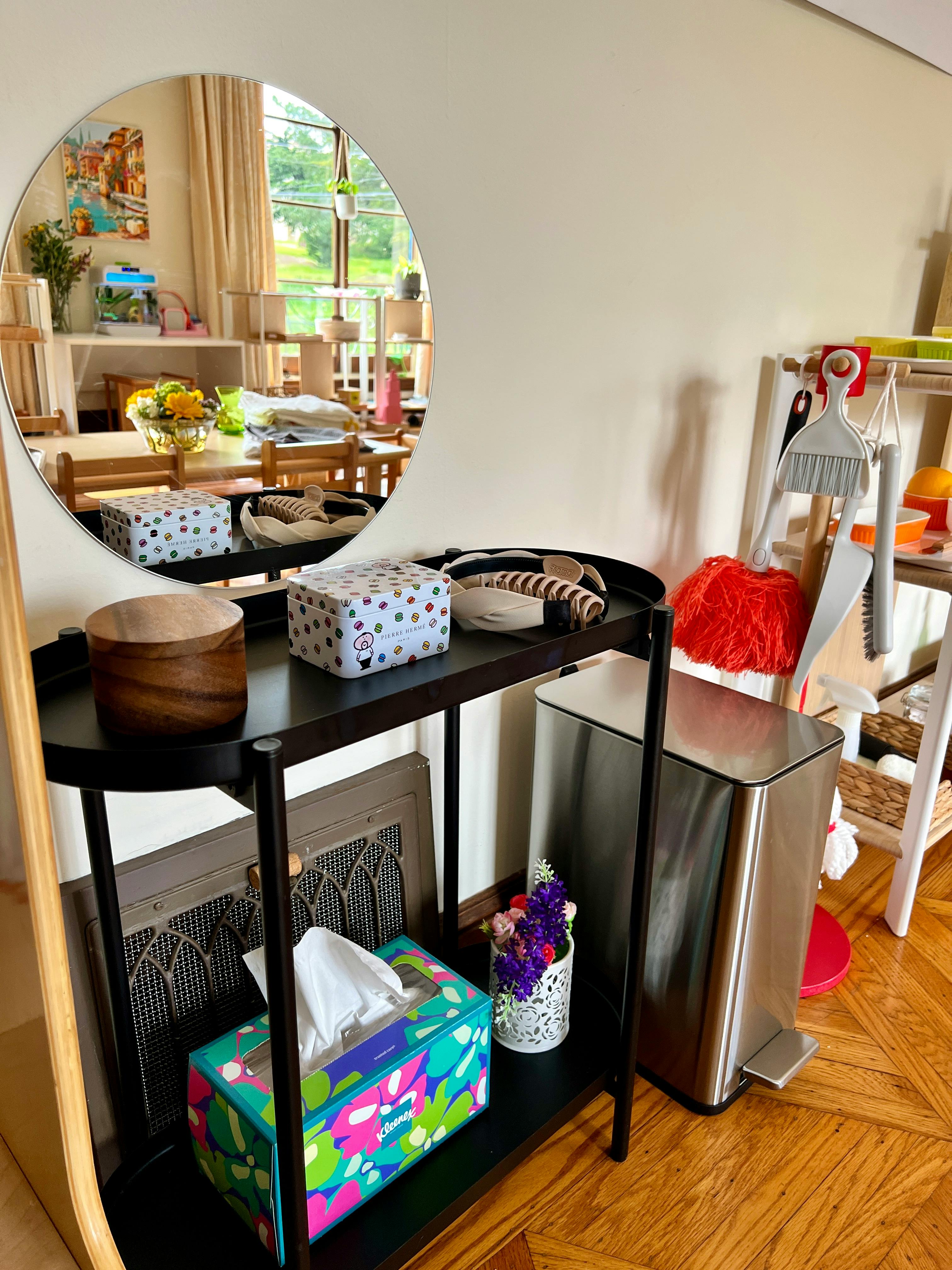 Round mirror reflecting a room with a table and chairs, next to a shelf with items