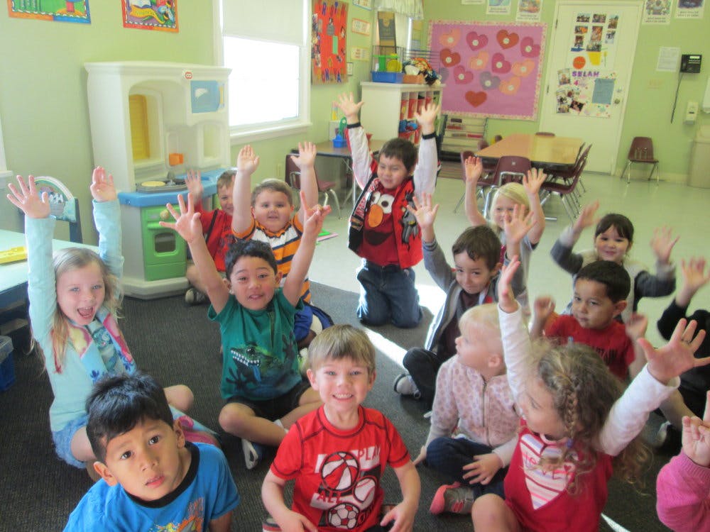 Group of children sitting on the floor with hands raised in a classroom