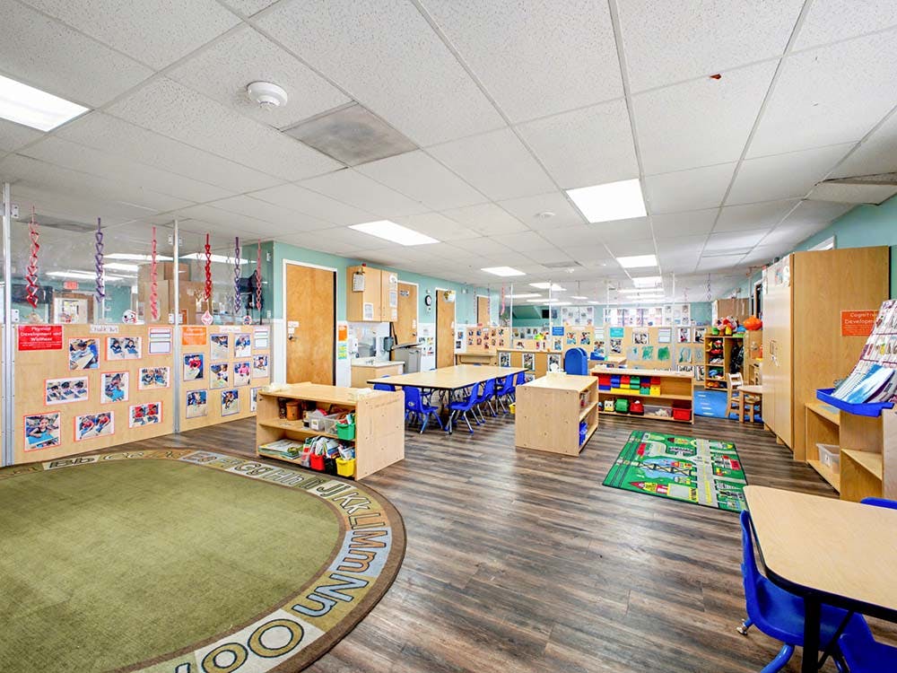 Classroom with tables, chairs, shelving units, and a large circular rug