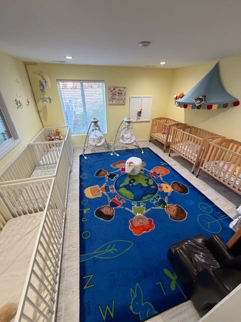 cribs, swings, and a child-themed rug in a childcare room