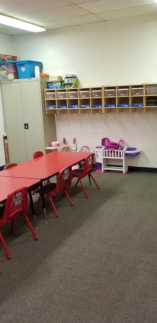 Classroom with red tables and chairs, storage shelves, and play furniture
