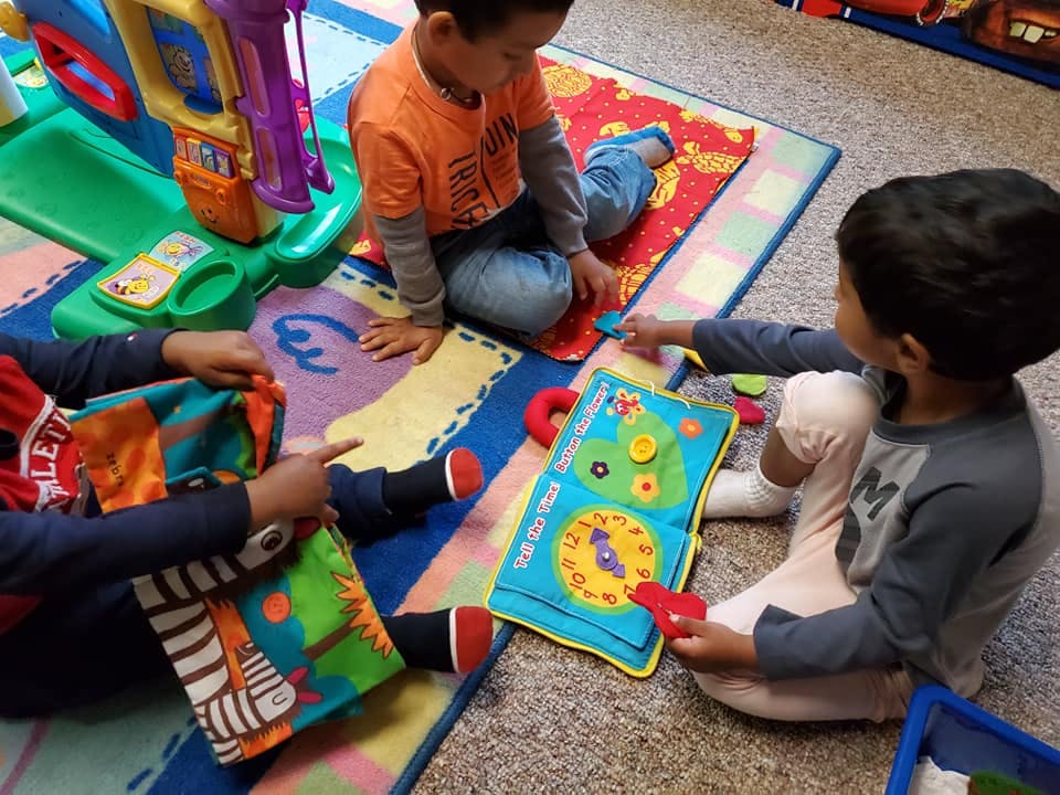 Three children playing with toys on a colorful mat