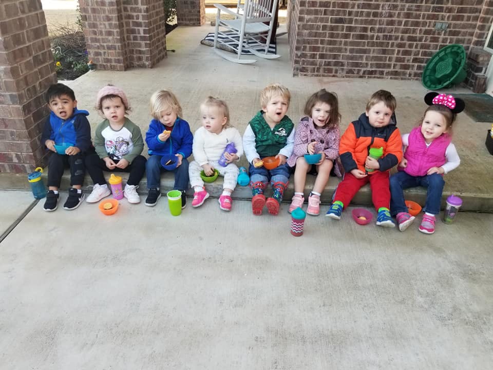 Seven children sitting in a row on a concrete surface