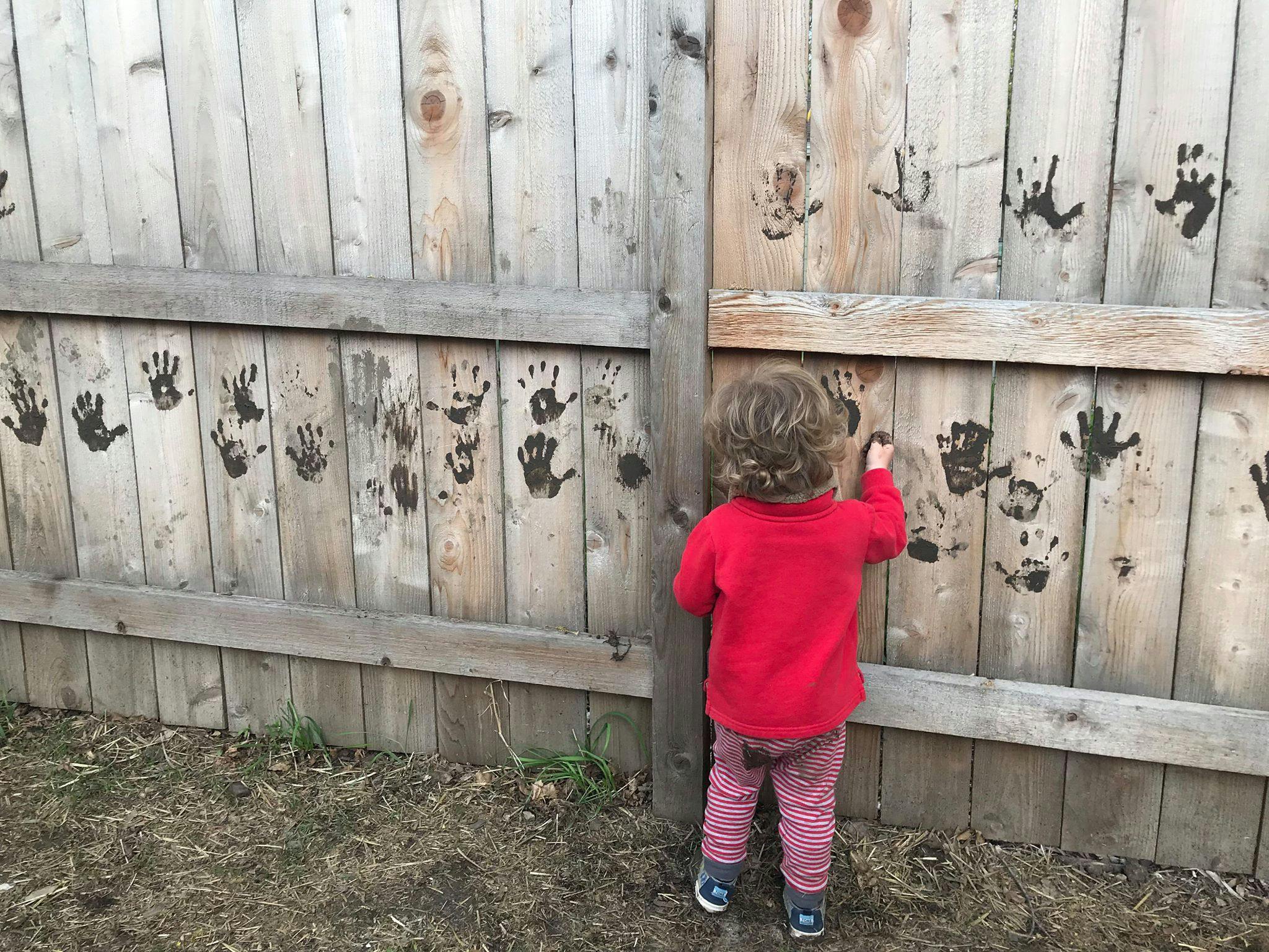 Child making handprints on a wooden fence